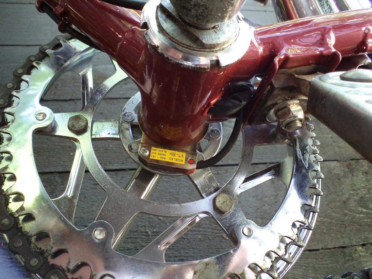 Dit is de trapsensor die de elektrische ondersteuning inschakelt. De magneetschijf heb ik zilverkleurig geverfd zodat hij niet teveel opvalt. Je ziet hier ook de bedrading van de accu's die in de zadeltas en zadelbuis zitten uit de buis van de trapas komen. De trapas zelf is niet dik dus er is voldoende ruimte voor de bedrading. De draden komen uit de zadelbuis en lopen langs de trapas, ik heb een beschermhuls om de trapas gemaakt zodat de draden niet tegen de trapas komen. Het gat onderin de buis heb ik er in gemaakt voor het peodercoaten, dus dat is netjes afgewerkt.